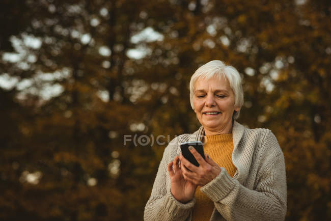 Mulher sênior usando um telefone inteligente em um parque ao amanhecer — Fotografia de Stock