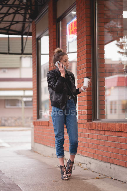 Schönes Mädchen, das mit dem Handy telefoniert, während es vor dem Einkaufszentrum Kaffee trinkt — Stockfoto