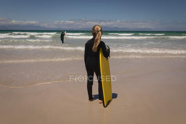 Fratelli in muta in piedi con tavola da surf in spiaggia — Foto stock