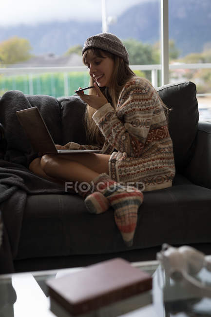 Frau benutzt Laptop beim Telefonieren im heimischen Wohnzimmer. — Stockfoto