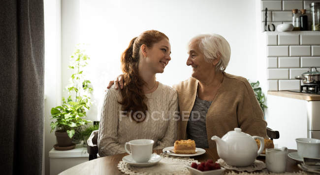 Abuela sonriente y nieta mirándose mientras están sentados en la sala de estar - foto de stock