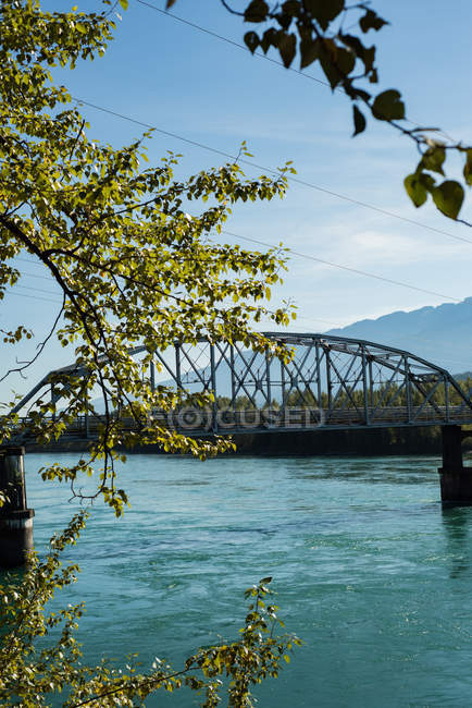 Metal bridge over the river surrounded with trees — Stock Photo