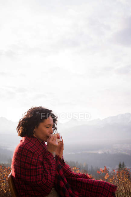 Caminhante feminina em cobertor tomando café em um dia ensolarado — Fotografia de Stock