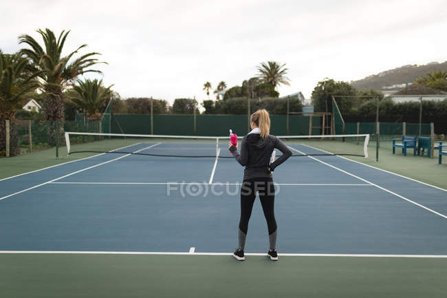 Вид ззаду жінки, що тримає пляшку води в тенісному корті — стокове фото