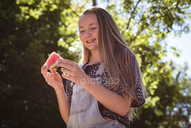 Усміхнена дівчина дивиться на шматочок кавуна в руках на відкритому повітрі . — стокове фото