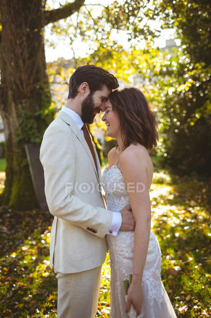 Усміхнена наречена і наречена обіймаються в саду в сонячний день — стокове фото