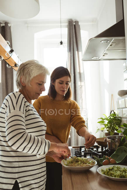 Mujer e hija mayores cocinando juntas en la cocina en casa - foto de stock