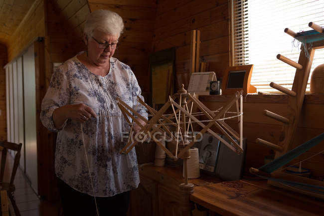 Donna anziana attiva che usa il telaio di tessitura in negozio — Foto stock