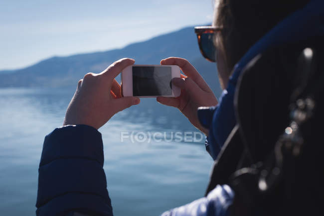Vue arrière de la femme prenant une photo avec un téléphone portable par une journée ensoleillée — Photo de stock