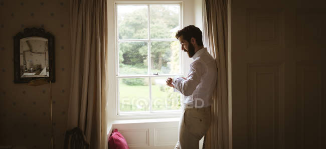 Homem verificando seu relógio perto da janela em casa — Fotografia de Stock