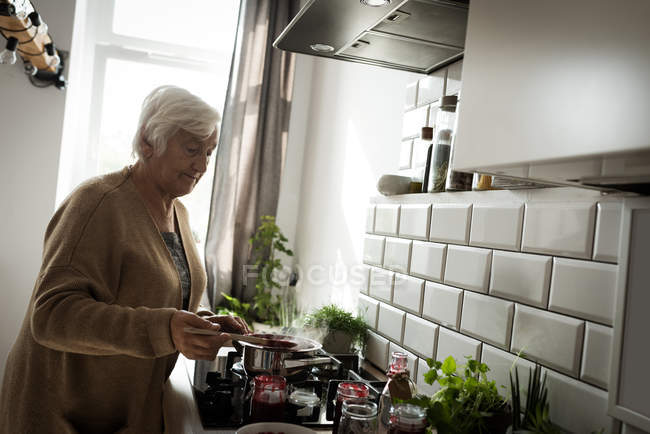 Mulher sênior cozinhar geléia de framboesa na cozinha em casa — Fotografia de Stock