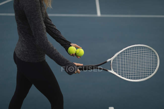Secção média da mulher segurando raquete e bola de tênis no campo de ténis — Fotografia de Stock