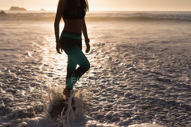 Fit woman standing in splashing sea water on beach at dusk. — Stock Photo