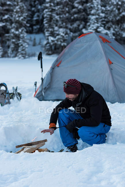 Uomo preparare falò vicino tenda nel bosco innevato durante l'inverno . — Foto stock