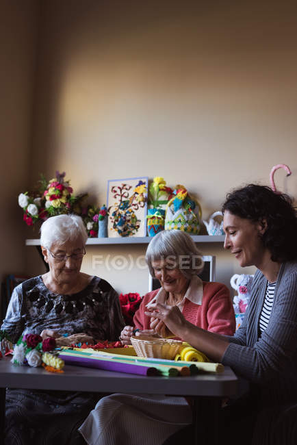Две пожилые женщины делают искусственный цветок со смотрителем в доме престарелых — стоковое фото
