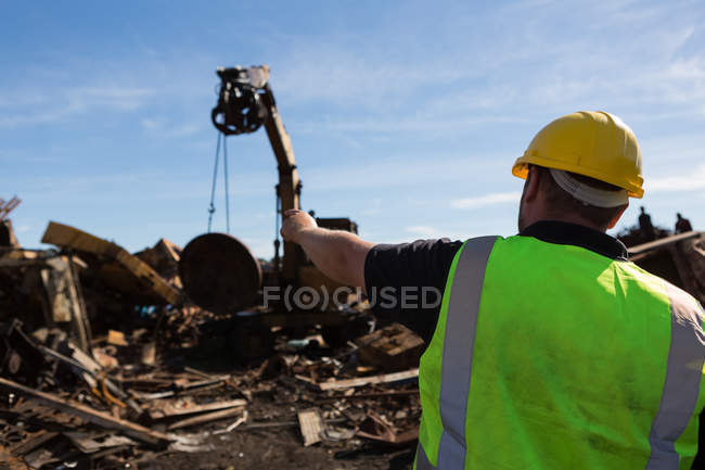 Rear view of worker pointing at the trash being lifted by crane — Stock Photo