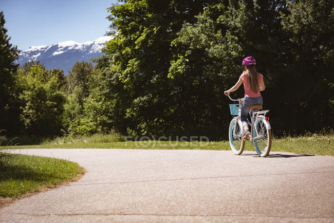 Rear view of girl in safety helmet riding bicycle on road. — Stock Photo