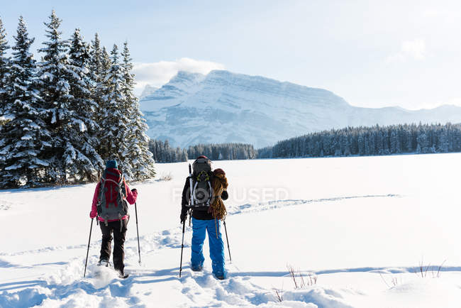 Pareja caminando junto con mochilas en el paisaje nevado durante el invierno . - foto de stock