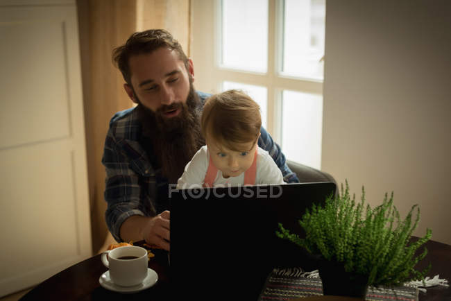 Père prendre un café pendant que le fils joue sur ordinateur portable à la maison — Photo de stock