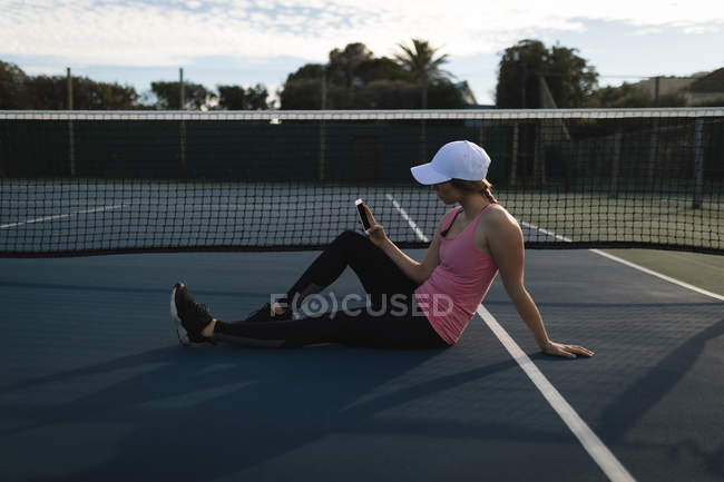 Junge Frau benutzt Handy auf Tennisplatz — Stockfoto
