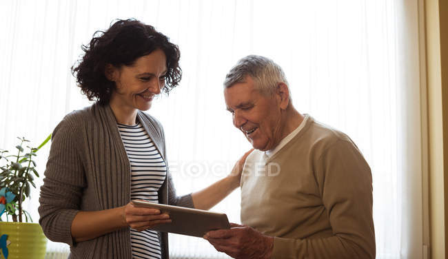 Gardien montrant tablette numérique à la femme âgée à la maison de soins infirmiers — Photo de stock
