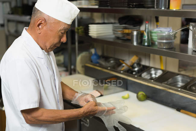 Senior chef wearing plastic gloves in kitchen at hotel — Stock Photo