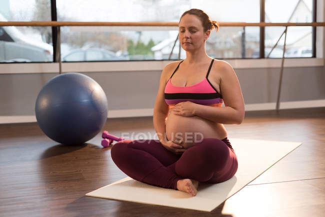 Mujer embarazada meditando mientras toca su vientre - foto de stock