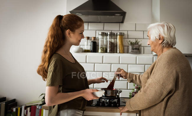 Grandmother and granddaughter cooking raspberry jam in kitchen at home — Stock Photo