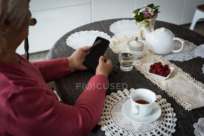 Пожилая женщина пользуется мобильным телефоном в гостиной дома — стоковое фото