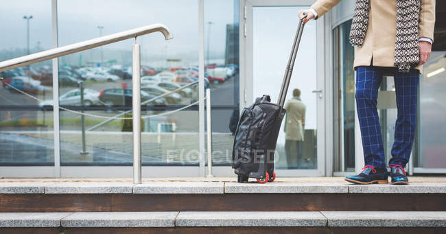 Baixa seção de homem de negócios saindo do hotel com bagagem — Fotografia de Stock