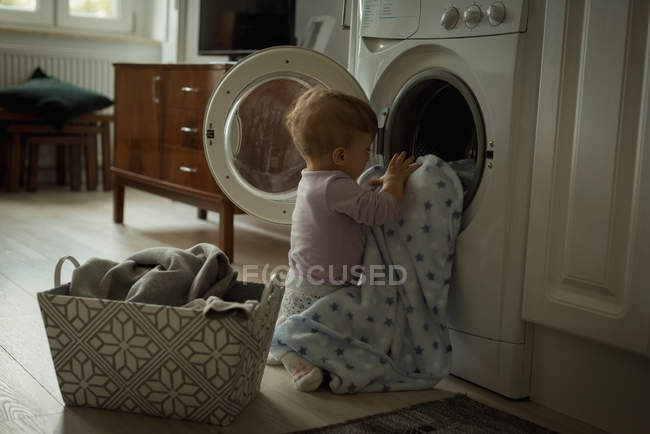 Младенец кладет одежду в стиральную машину дома — стоковое фото