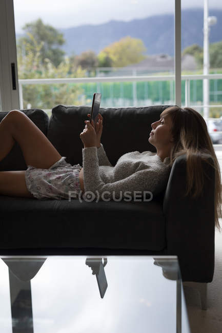 Mujer joven usando tableta digital en el sofá en la sala de estar en casa . - foto de stock