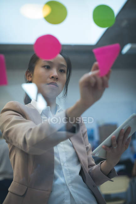 Executive sticking adhesive note on glass wall in office — Stock Photo