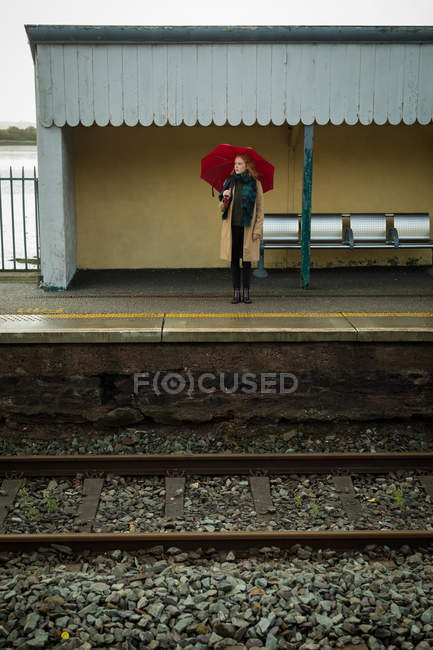 Молода жінка стоїть з парасолькою на залізничному вокзалі — стокове фото