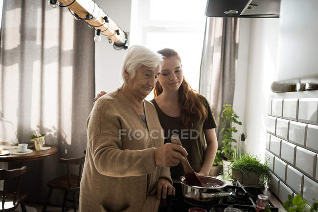 Großmutter und Enkelin kochen Himbeermarmelade in der heimischen Küche — Stockfoto