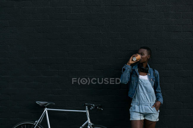 Молодая женщина пьет кофе у стены — стоковое фото