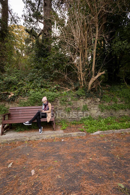 Жінка сидить на лавці і використовує мобільний телефон в парку — стокове фото