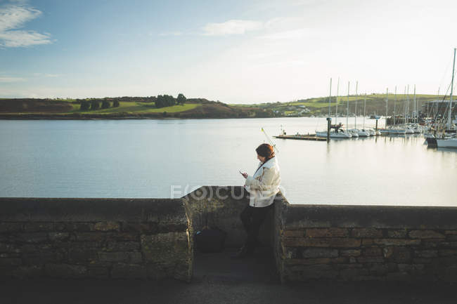 Mulher usando telefone celular perto da ribeira pela água . — Fotografia de Stock