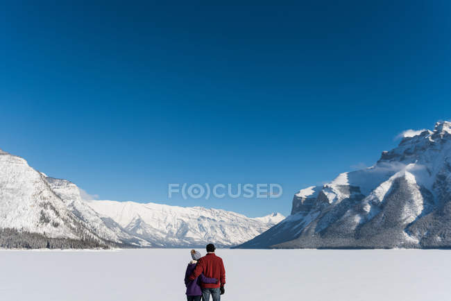 Vista trasera de la pareja de pie y abrazándose en el paisaje nevado . - foto de stock