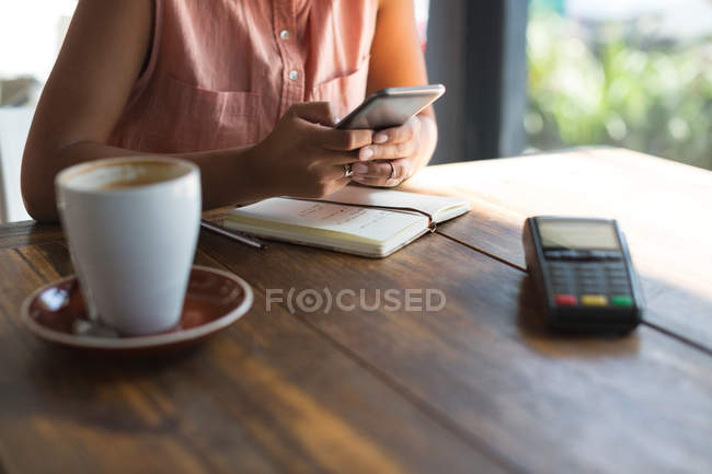 Mid section of teenage girl using mobile phone beside payment terminal in restaurant — Stock Photo