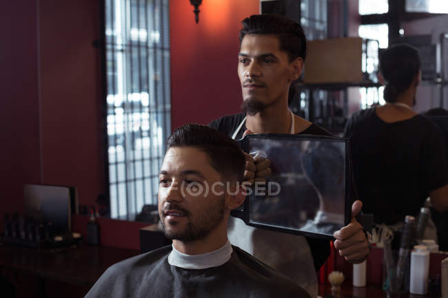 Man looking his new hair cut in the mirror at barbershop — Stock Photo