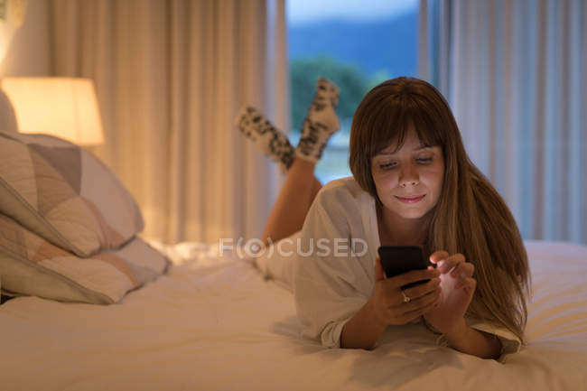 Frau benutzte Handy auf dem Bett im Schlafzimmer zu Hause. — Stockfoto