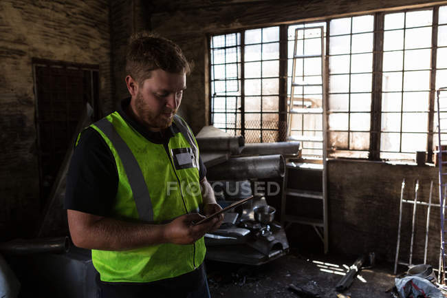 Trabajador concentrado usando tableta digital en el depósito de chatarra - foto de stock