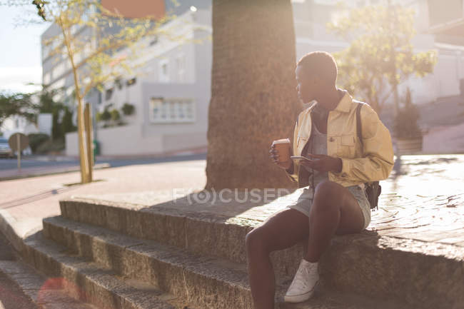 Woman having coffee while using mobile phone in city — Stock Photo