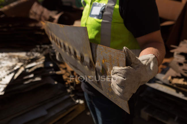 Mid-section of worker holding a rusty metal bar in the scrapyard — Stock Photo