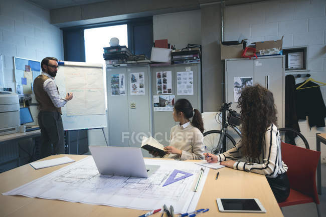 Executive giving presentation to coworker over flip chart in office — Stock Photo