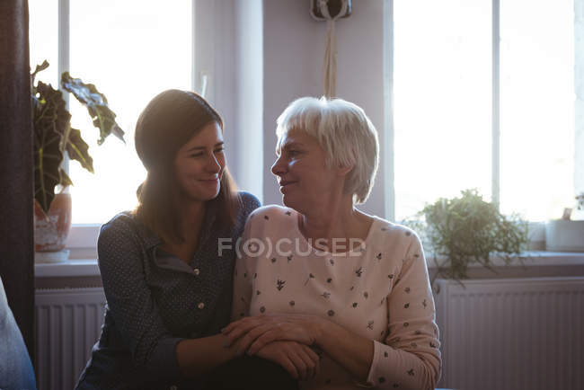 Donna anziana e figlia sedute sul divano che si abbracciano nel soggiorno di casa — Foto stock
