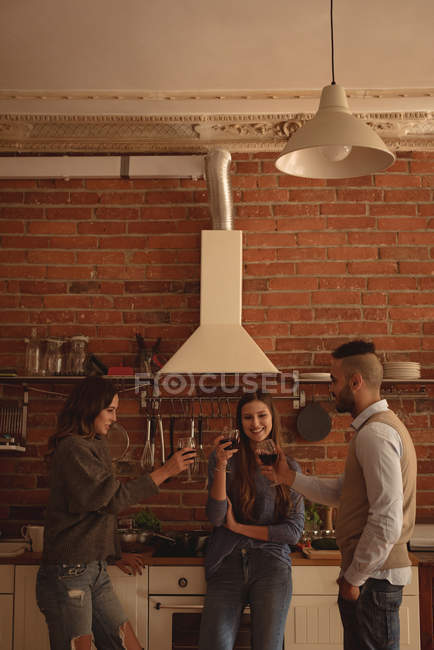 Glückliche Freunde stoßen zu Hause in der Küche auf Wein an — Stockfoto