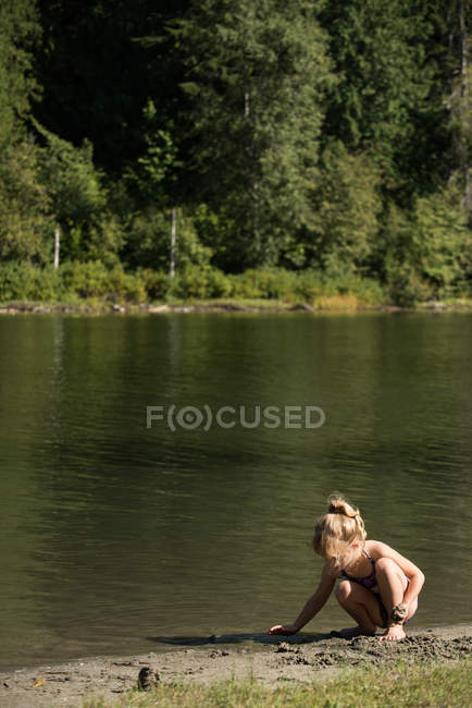 Ragazza che gioca con la sabbia vicino al fiume in una giornata di sole — Foto stock