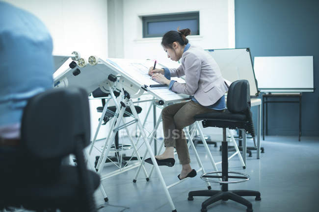 Female executive working over drafting table in office — Stock Photo